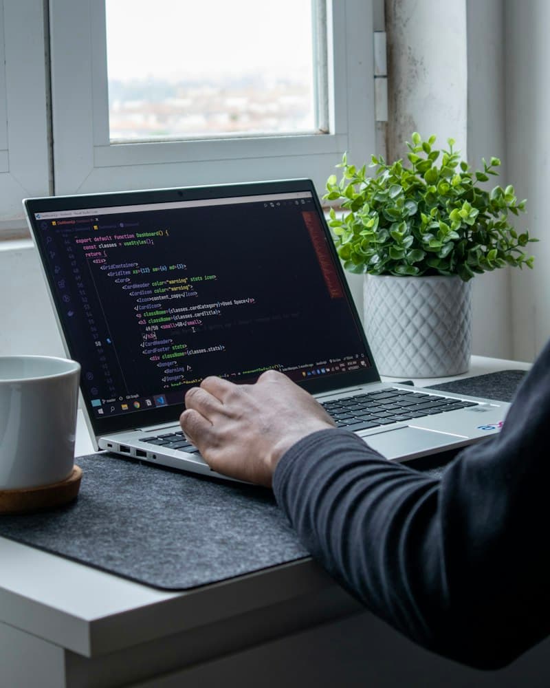 Hands typing code on a laptop by a window