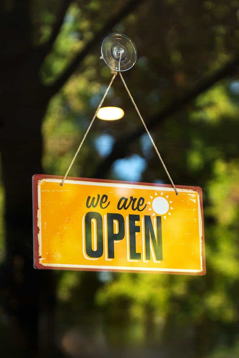 A yellow 'we are open' sign hanging in a shop window